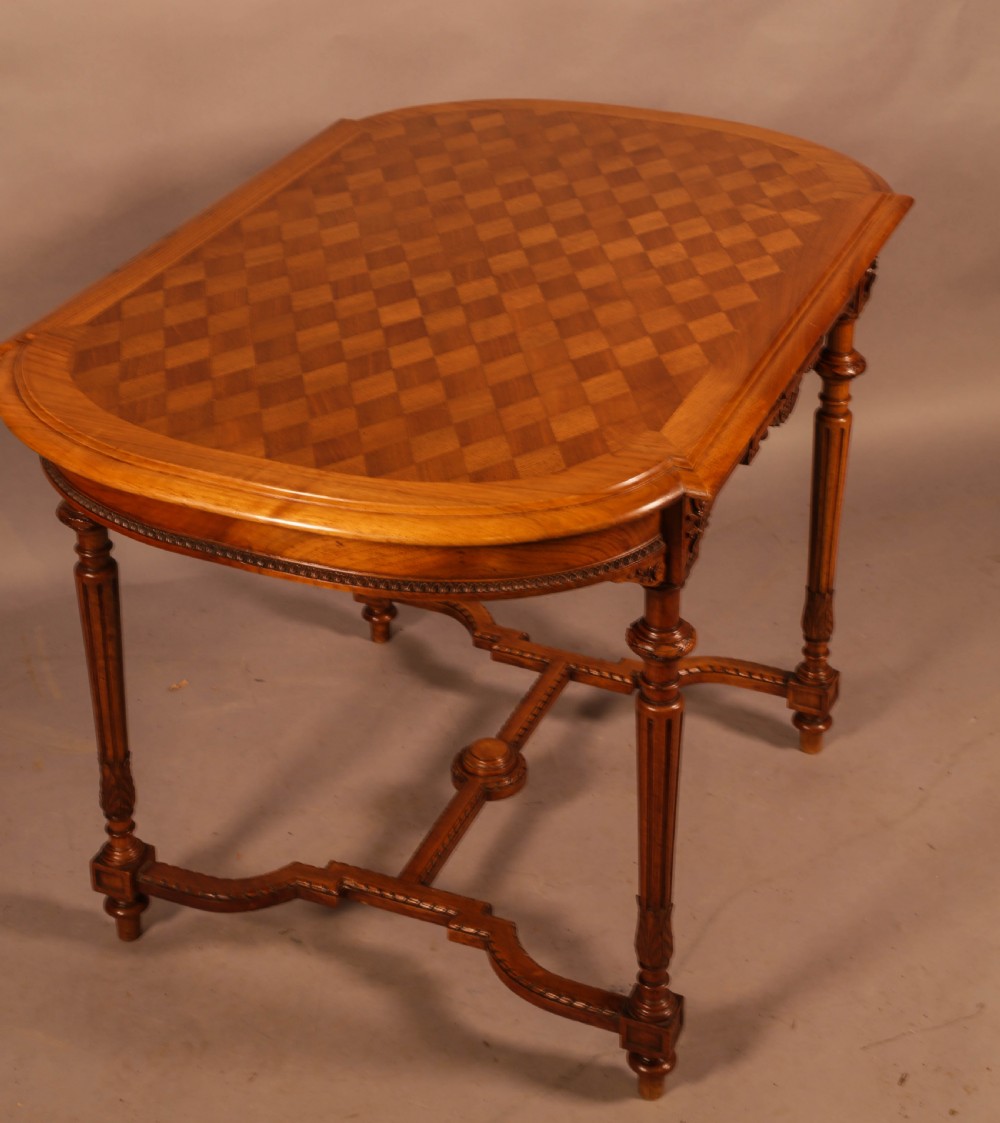 An antique French walnut window table featuring a geometric parquetry top, carved aprons, turned fluted legs, and a shaped cross-stretcher. View VI