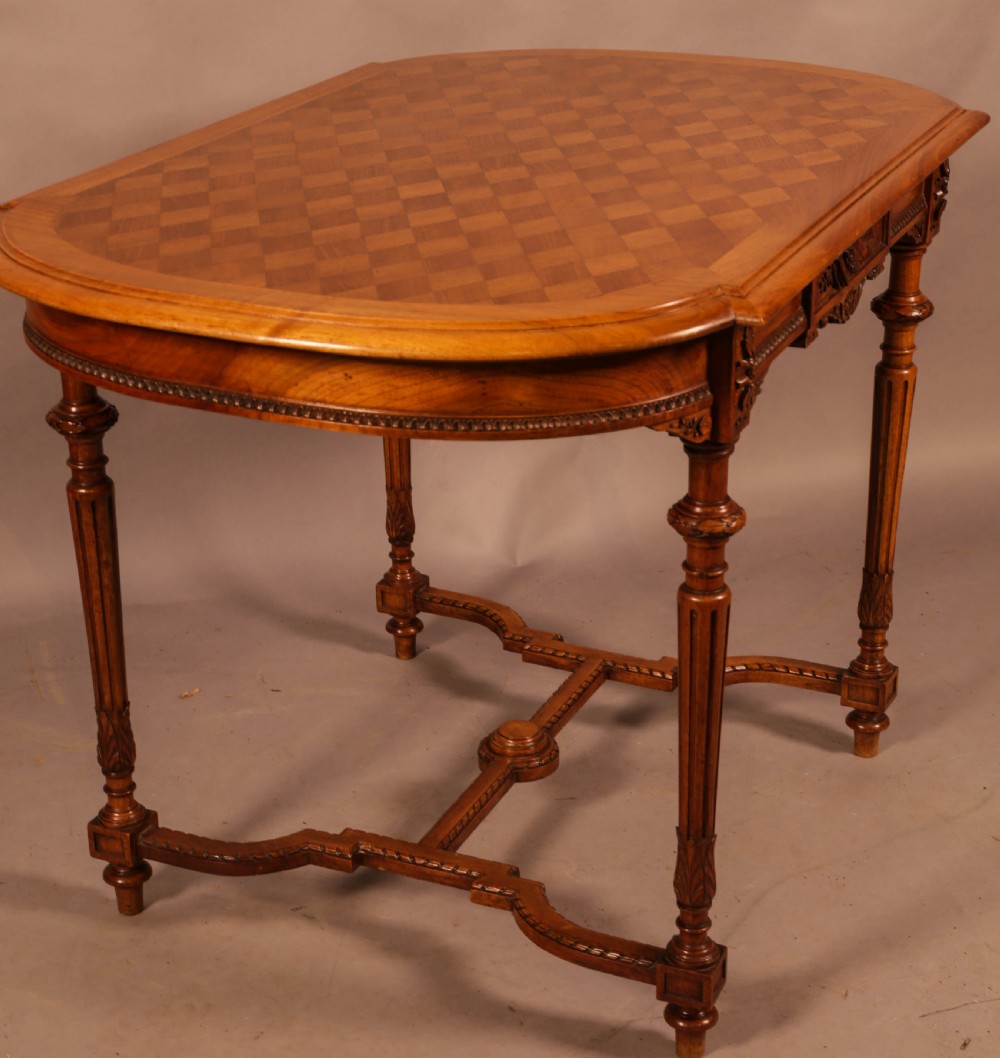 An antique French walnut window table featuring a geometric parquetry top, carved aprons, turned fluted legs, and a shaped cross-stretcher. View VII