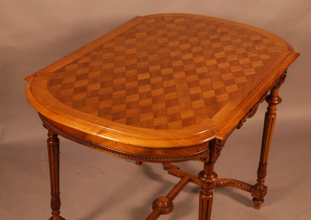 An antique French walnut window table featuring a geometric parquetry top, carved aprons, turned fluted legs, and a shaped cross-stretcher. View VIII