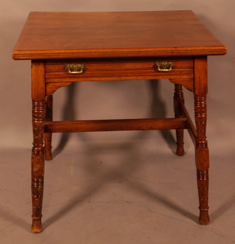 An Aesthetic Movement warm brown walnut occasional table with turned legs, a single drawer featuring brass handles, and a lower H-stretcher.
