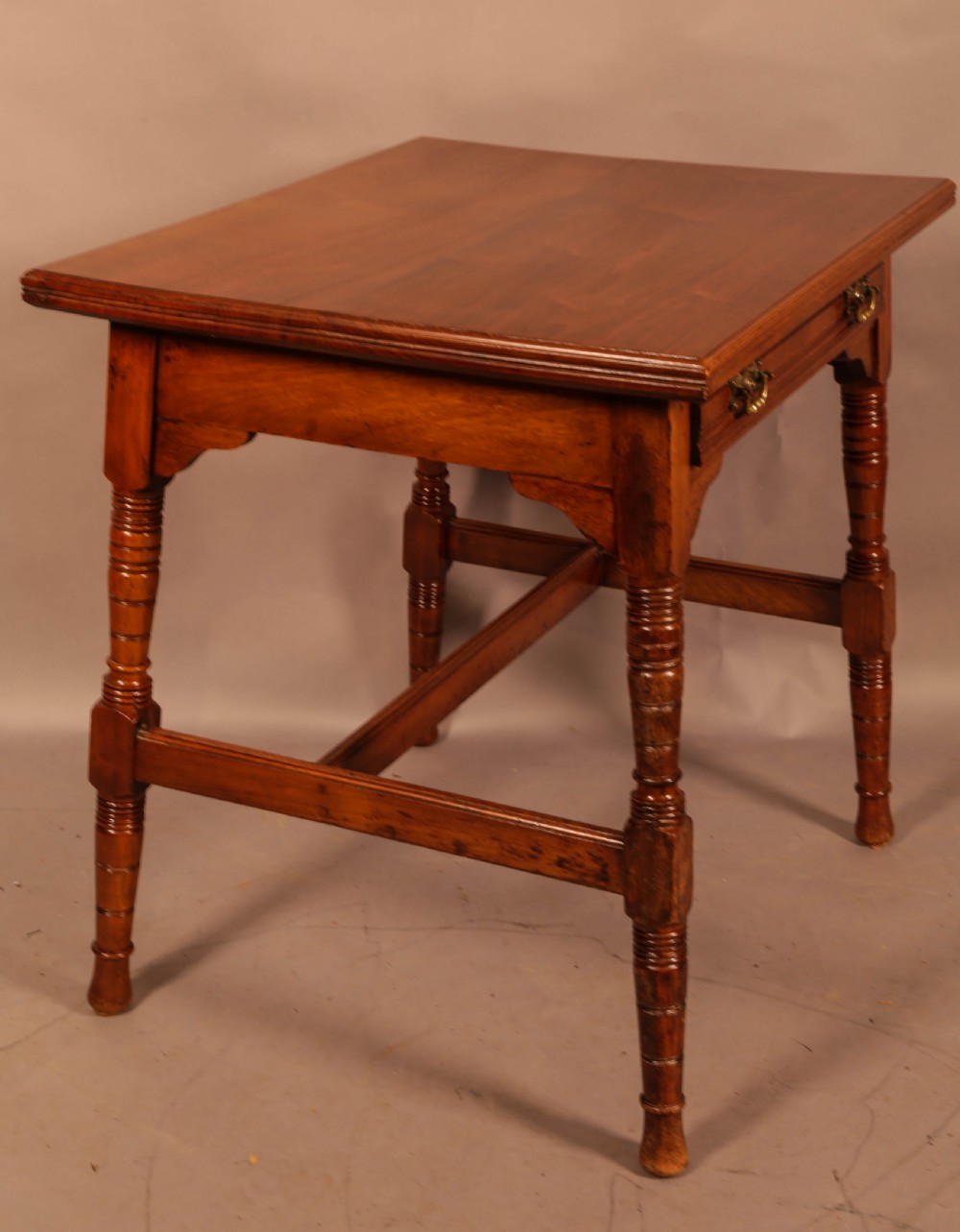 An Aesthetic Movement warm brown walnut occasional table with turned legs, a single drawer featuring brass handles, and a lower H-stretcher. View VI