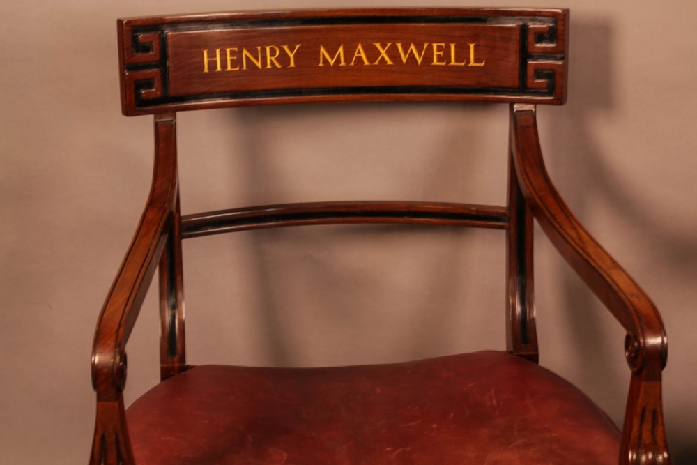 A pair of Regency mahogany carver chairs featuring red leather seats, sabre legs, ebony Greek key inlay, and the name Henry Maxwell gilt-stamped across the top rails. View II