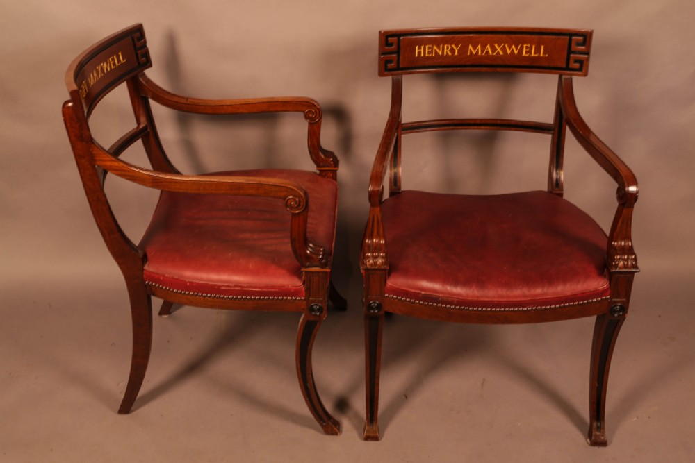 A pair of Regency mahogany carver chairs featuring red leather seats, sabre legs, ebony Greek key inlay, and the name Henry Maxwell gilt-stamped across the top rails. View III