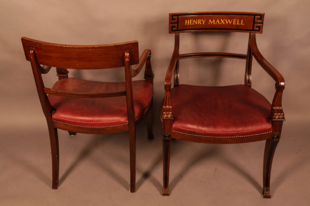 A pair of Regency mahogany carver chairs featuring red leather seats, sabre legs, ebony Greek key inlay, and the name Henry Maxwell gilt-stamped across the top rails. View IV