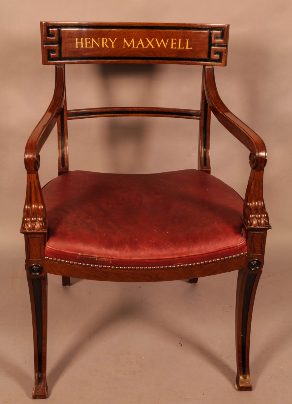 A pair of Regency mahogany carver chairs featuring red leather seats, sabre legs, ebony Greek key inlay, and the name Henry Maxwell gilt-stamped across the top rails. View V