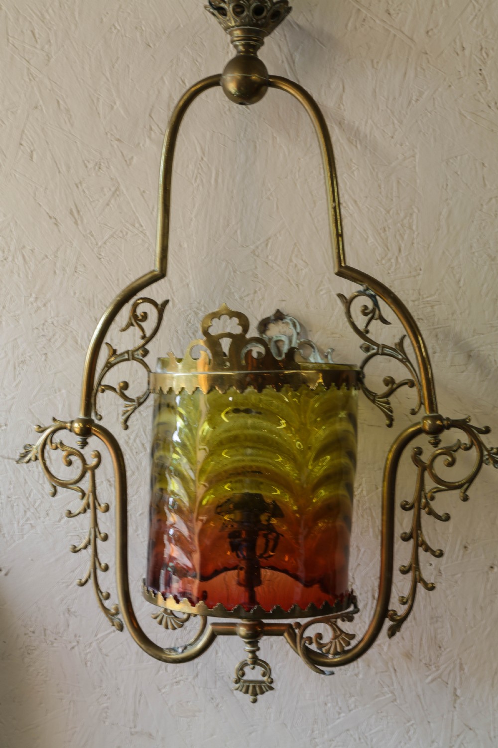 Victorian brass hanging lantern featuring an ornate scrollwork frame enclosing a cylindrical shade with graded yellow and red glass.
