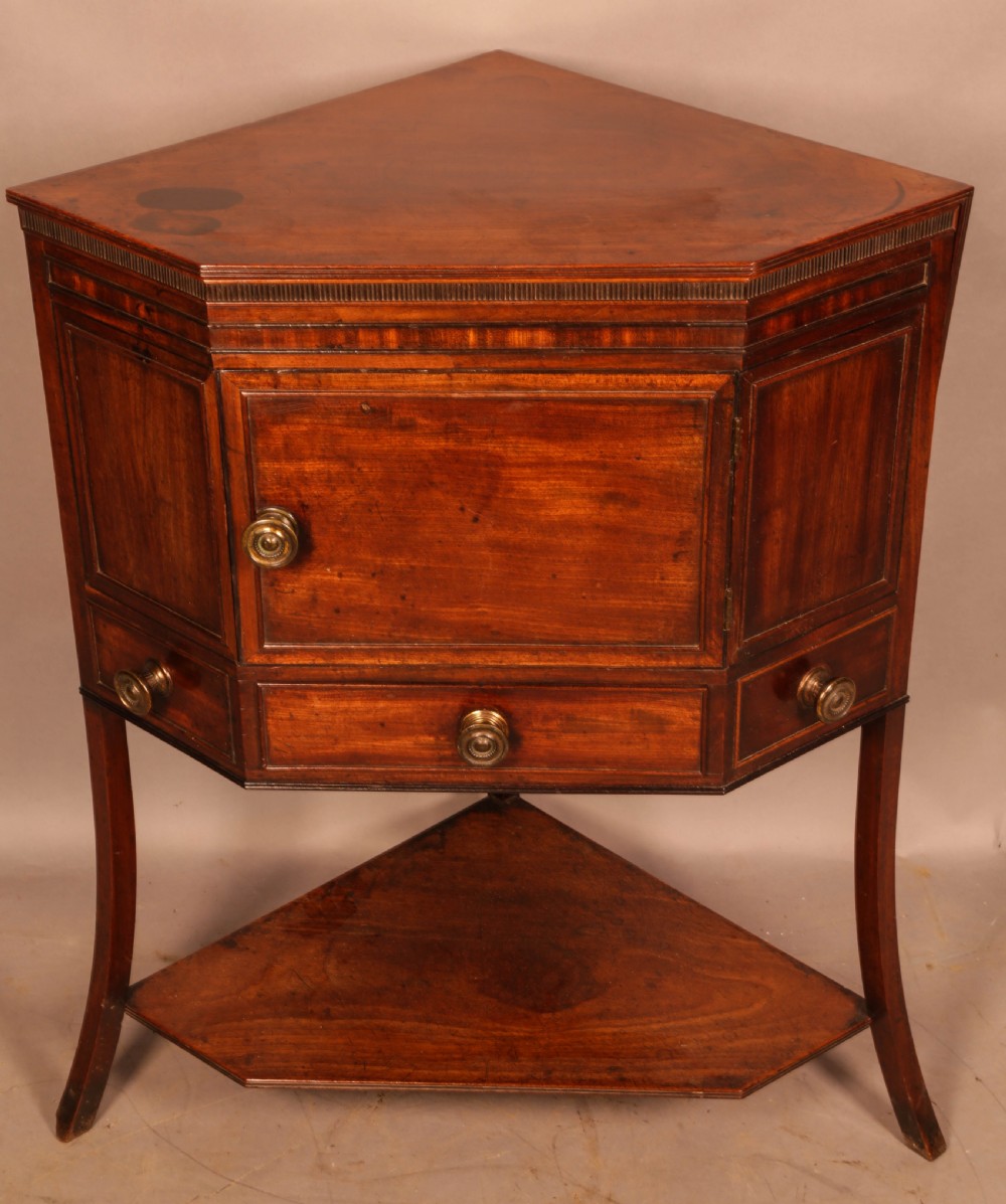 An 18th-century Georgian mahogany corner washstand featuring a hinged splashback, central basin opening, single cupboard door, brass knob handles, and a lower undertier shelf. View II