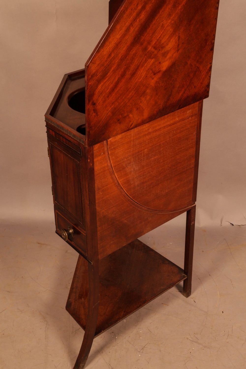 An 18th-century Georgian mahogany corner washstand featuring a hinged splashback, central basin opening, single cupboard door, brass knob handles, and a lower undertier shelf. View IV