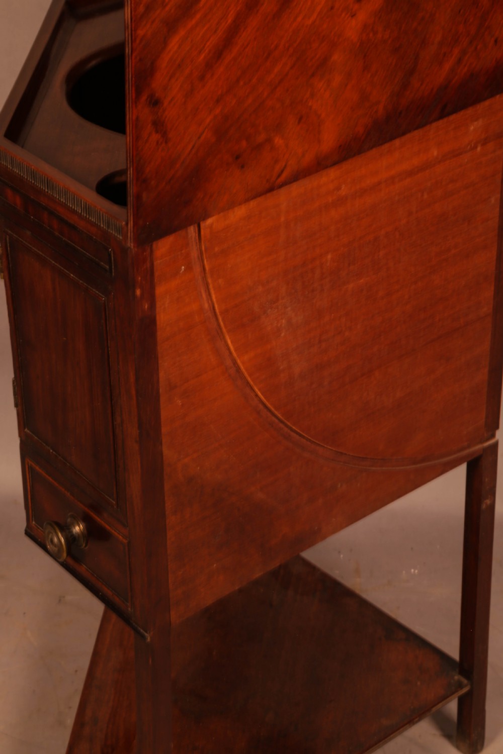 An 18th-century Georgian mahogany corner washstand featuring a hinged splashback, central basin opening, single cupboard door, brass knob handles, and a lower undertier shelf. View V