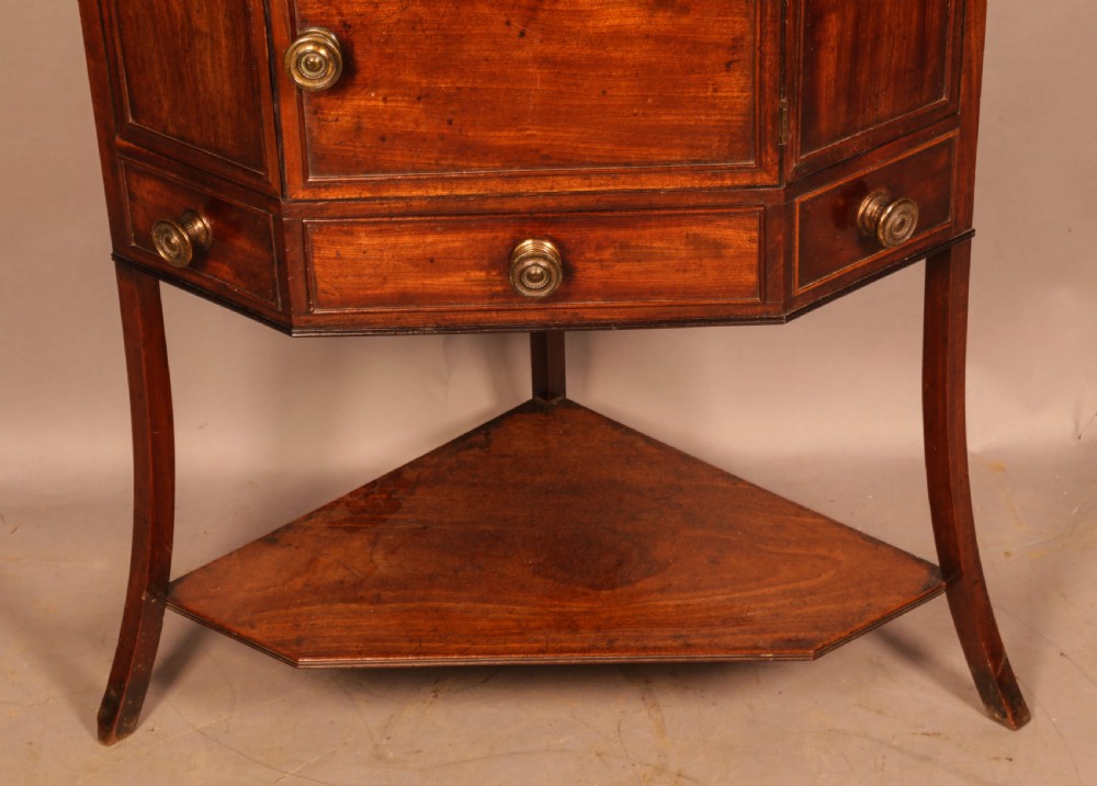 An 18th-century Georgian mahogany corner washstand featuring a hinged splashback, central basin opening, single cupboard door, brass knob handles, and a lower undertier shelf. View VII