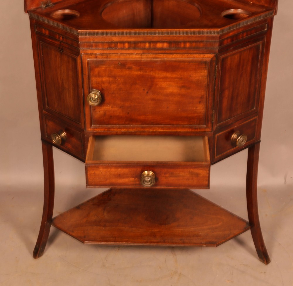 An 18th-century Georgian mahogany corner washstand featuring a hinged splashback, central basin opening, single cupboard door, brass knob handles, and a lower undertier shelf. View VIII