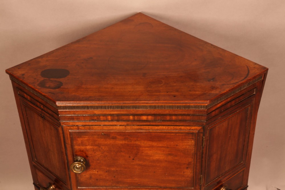 An 18th-century Georgian mahogany corner washstand featuring a hinged splashback, central basin opening, single cupboard door, brass knob handles, and a lower undertier shelf. View X