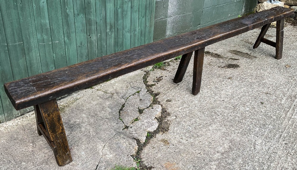 A long 18th-century dark oak trestle bench with a plank seat and splayed supports.