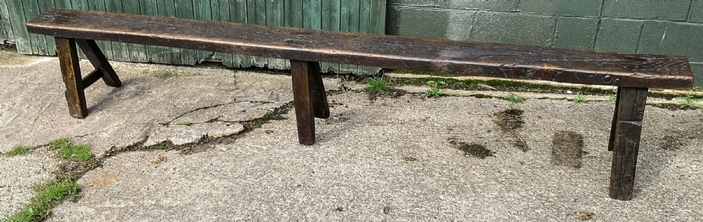 A long 18th-century dark oak trestle bench with a plank seat and splayed supports. View II