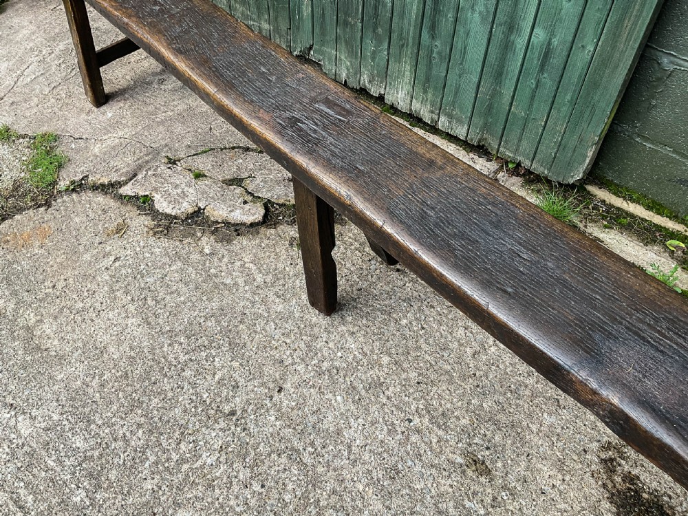 A long 18th-century dark oak trestle bench with a plank seat and splayed supports. View V