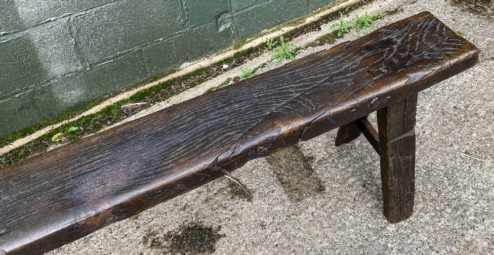 A long 18th-century dark oak trestle bench with a plank seat and splayed supports. View VI