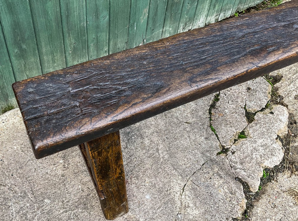 A long 18th-century dark oak trestle bench with a plank seat and splayed supports. View VII