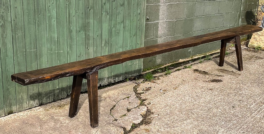 An 18th-century long solid oak trestle bench featuring a thick timber top and four splayed legs.