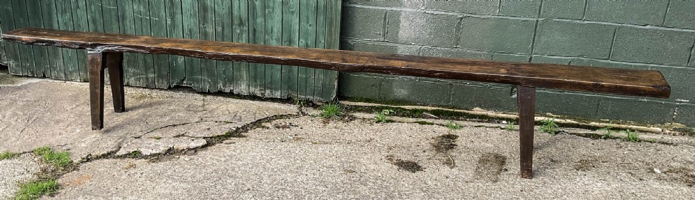 An 18th-century long solid oak trestle bench featuring a thick timber top and four splayed legs. View II