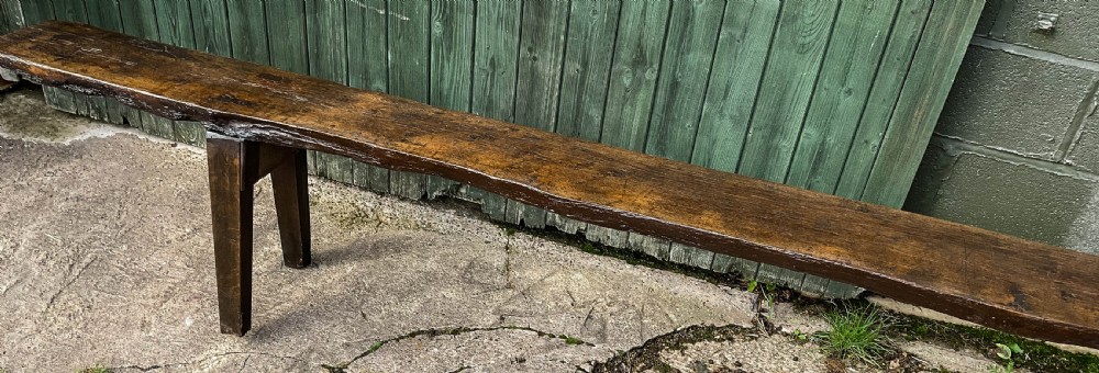 An 18th-century long solid oak trestle bench featuring a thick timber top and four splayed legs. View III