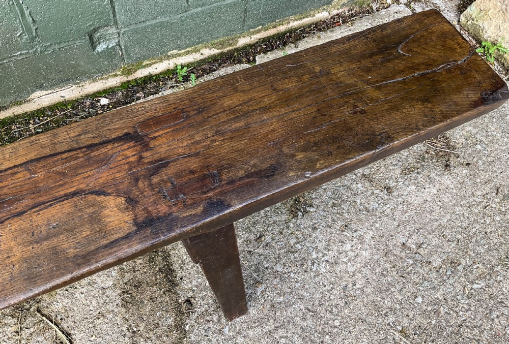 An 18th-century long solid oak trestle bench featuring a thick timber top and four splayed legs. View V