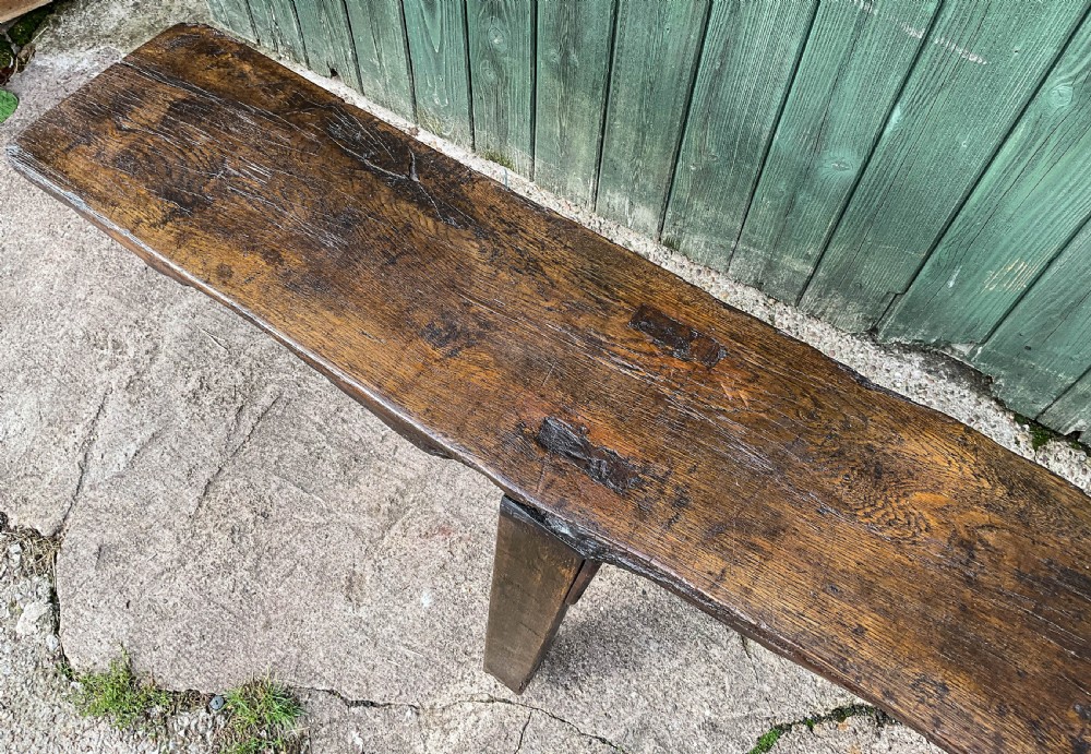 An 18th-century long solid oak trestle bench featuring a thick timber top and four splayed legs. View VI