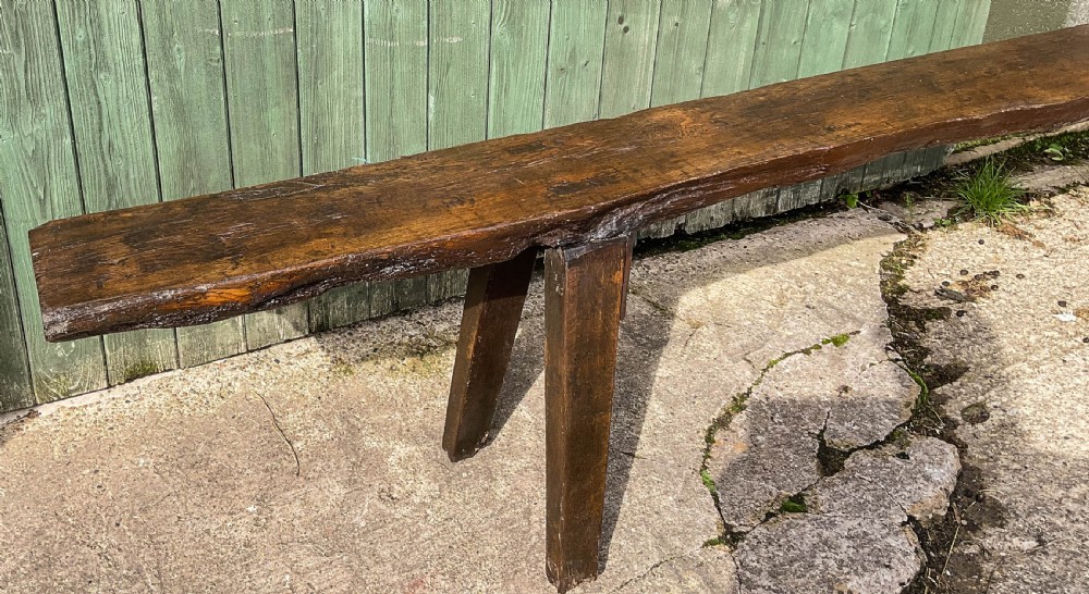 An 18th-century long solid oak trestle bench featuring a thick timber top and four splayed legs. View VII