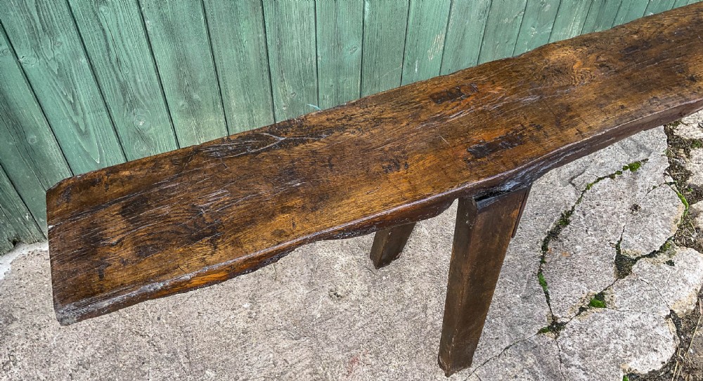 An 18th-century long solid oak trestle bench featuring a thick timber top and four splayed legs. View VIII