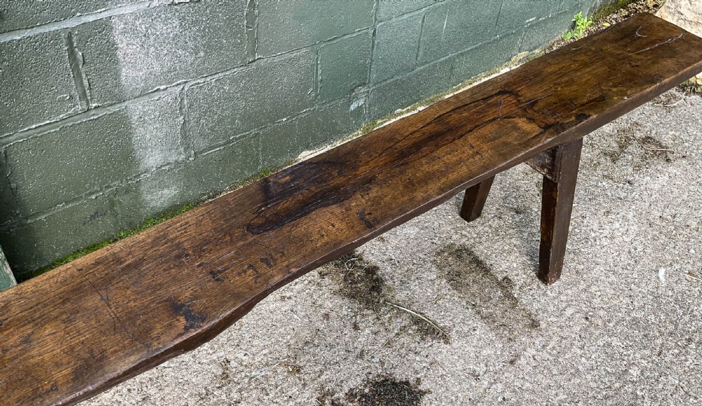 An 18th-century long solid oak trestle bench featuring a thick timber top and four splayed legs. View X