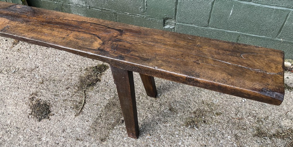 An 18th-century long solid oak trestle bench featuring a thick timber top and four splayed legs. View XI