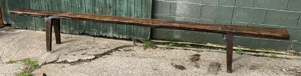 An 18th-century long solid oak trestle bench featuring a thick timber top and four splayed legs. View XII
