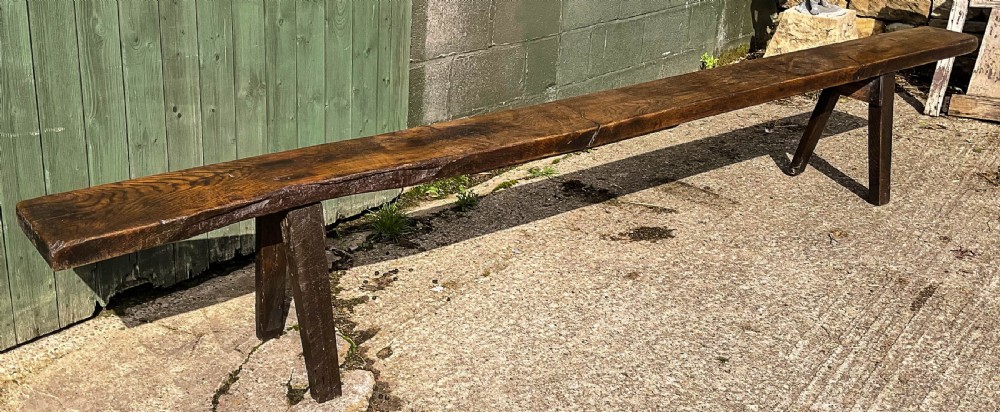 An exceptionally long 18th-century dark oak bench with a single-plank seat and splayed rectangular legs. View II