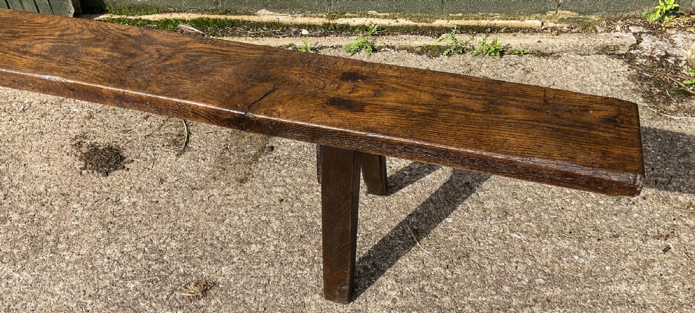 An exceptionally long 18th-century dark oak bench with a single-plank seat and splayed rectangular legs. View III
