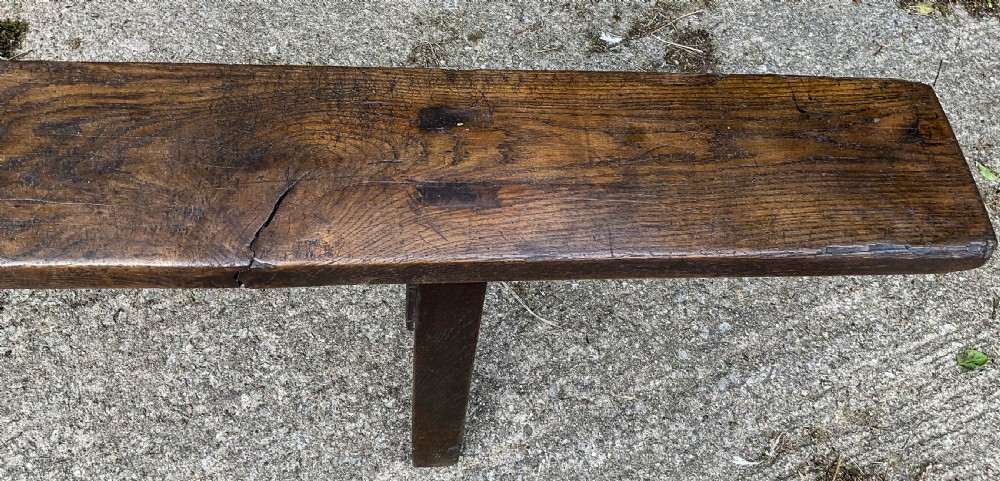 An exceptionally long 18th-century dark oak bench with a single-plank seat and splayed rectangular legs. View V