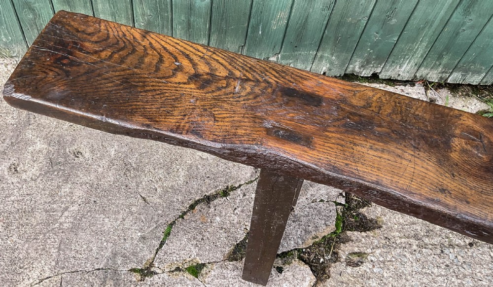 An exceptionally long 18th-century dark oak bench with a single-plank seat and splayed rectangular legs. View VII