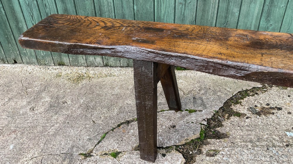 An exceptionally long 18th-century dark oak bench with a single-plank seat and splayed rectangular legs. View IX