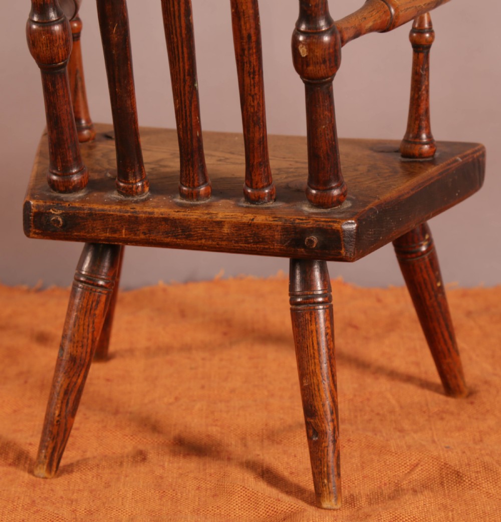 An antique wooden childrens spindle-back armchair featuring a solid saddle seat, turned armrests, and splayed legs with a warm brown patinated finish. View IV