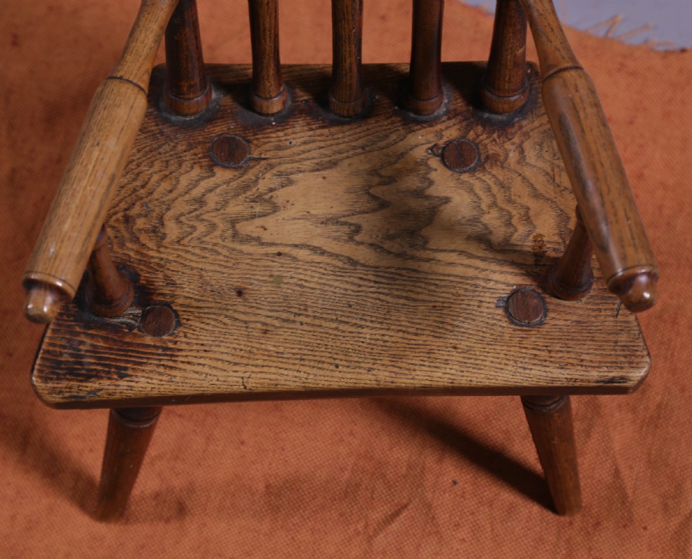 An antique wooden childrens spindle-back armchair featuring a solid saddle seat, turned armrests, and splayed legs with a warm brown patinated finish. View VIII