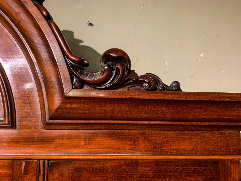 A 19th-century mahogany library bookcase featuring a carved arch pediment, glazed upper doors filled with books, and panelled cupboard doors below. View XI