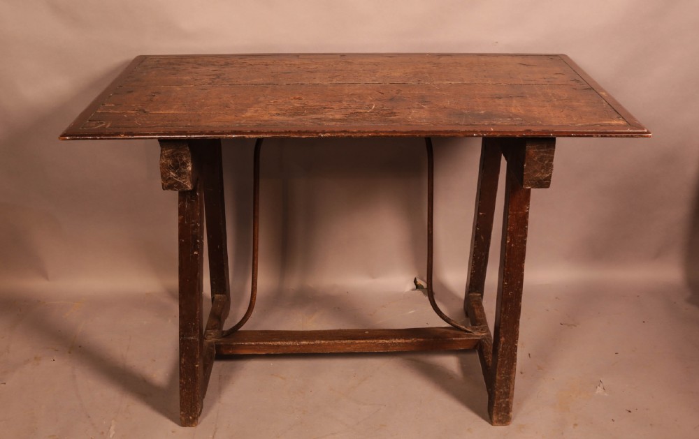 An antique dark timber trestle side table featuring a plank top supported by splayed legs and curved wrought iron stretchers.