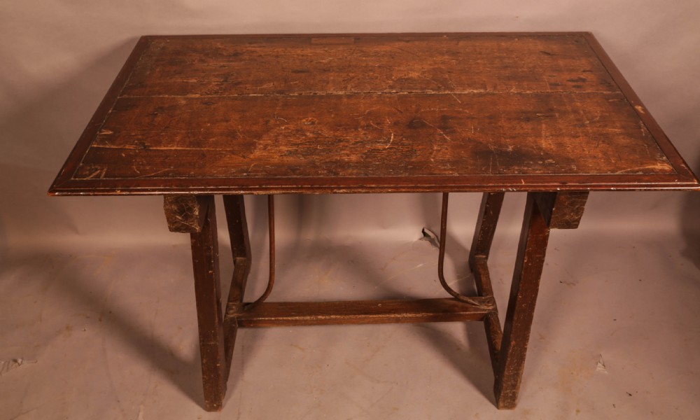 An antique dark timber trestle side table featuring a plank top supported by splayed legs and curved wrought iron stretchers. View II