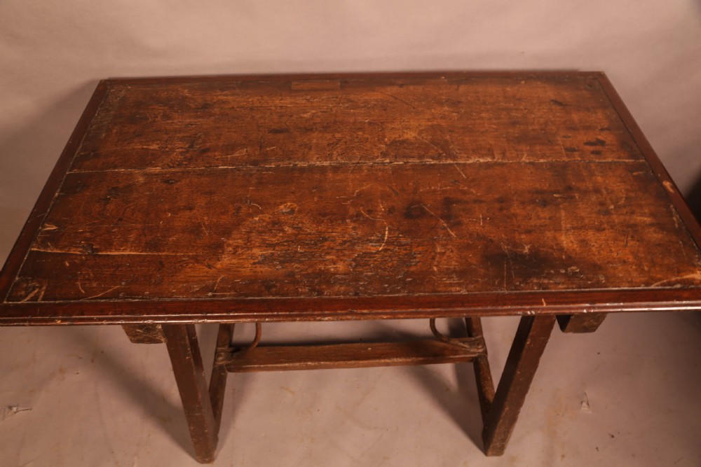 An antique dark timber trestle side table featuring a plank top supported by splayed legs and curved wrought iron stretchers. View III