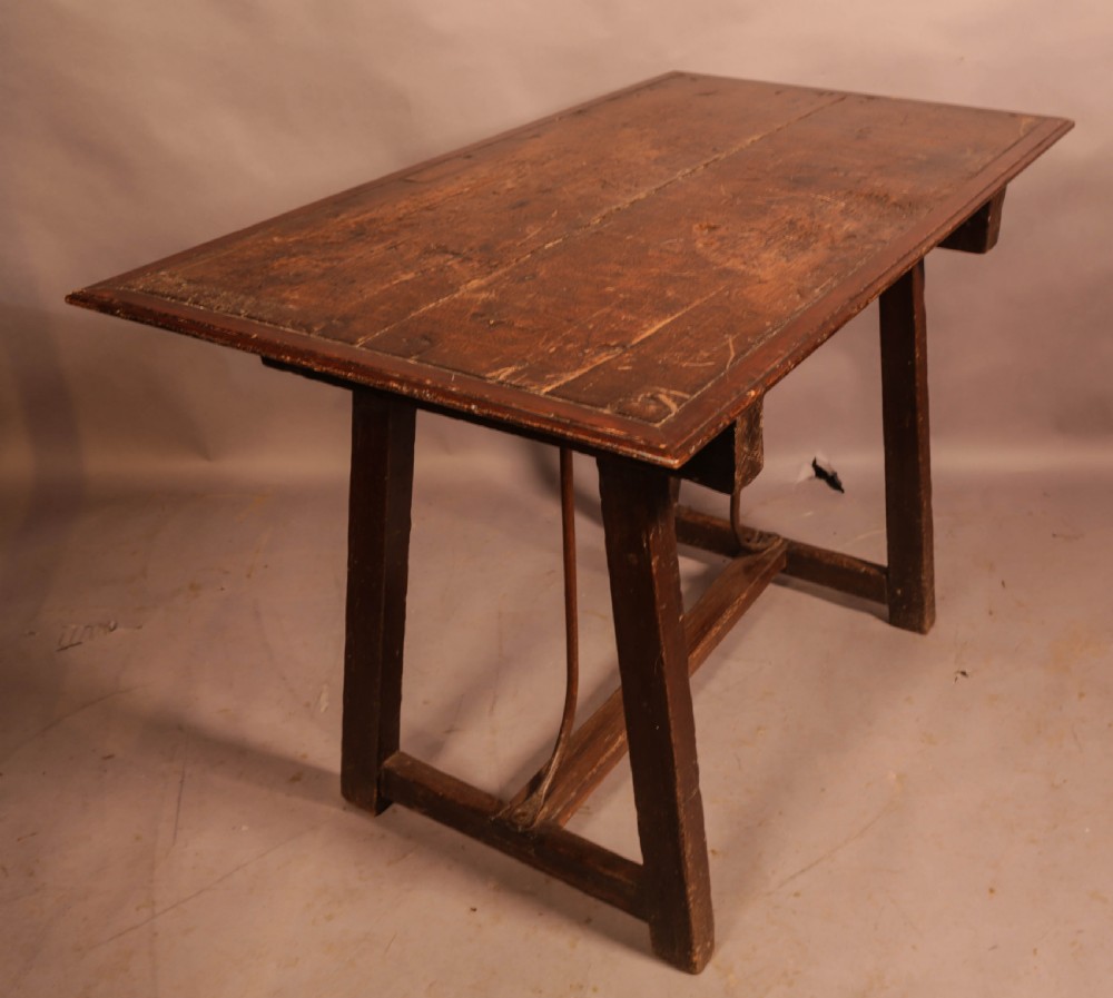 An antique dark timber trestle side table featuring a plank top supported by splayed legs and curved wrought iron stretchers. View V