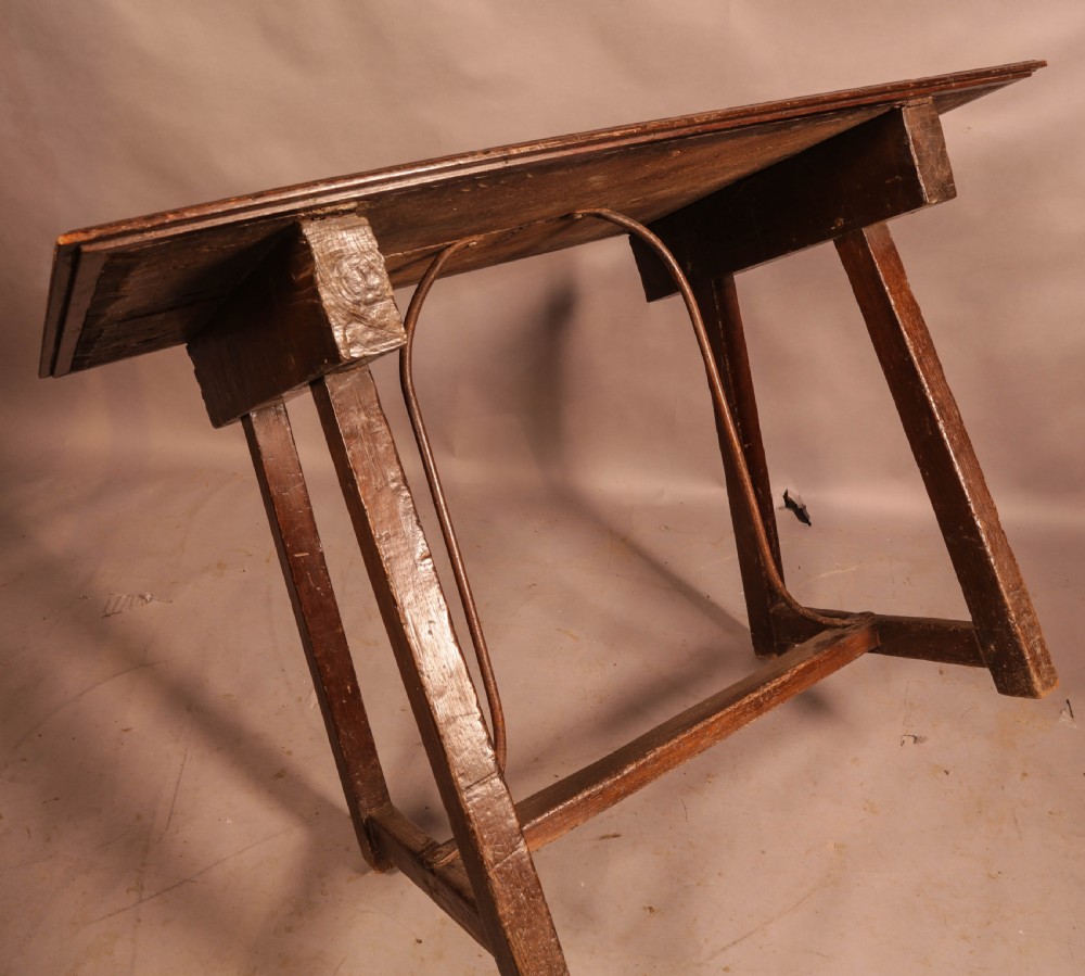 An antique dark timber trestle side table featuring a plank top supported by splayed legs and curved wrought iron stretchers. View VI