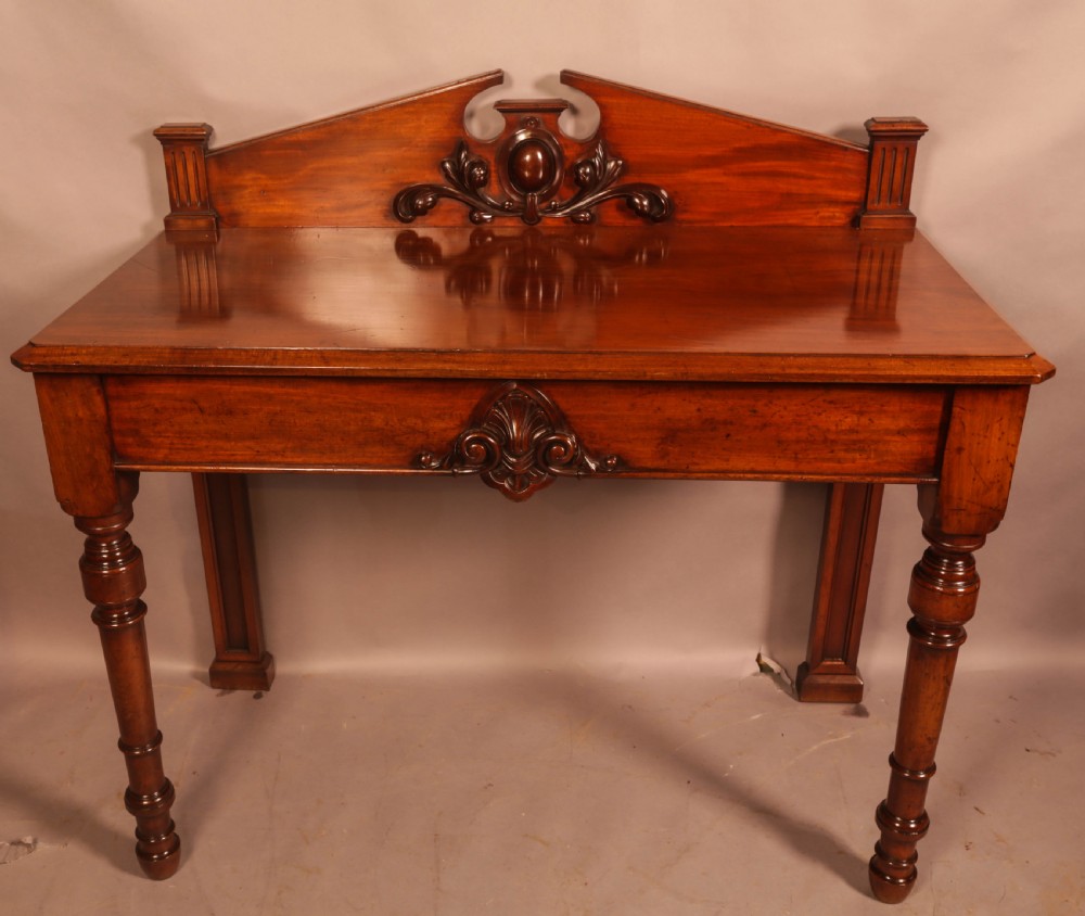 A Victorian mahogany serving table featuring a carved decorative backboard and turned front legs.