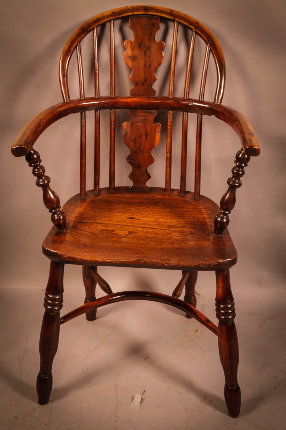 An antique 19th-century yew wood Windsor armchair featuring a hoop back, pierced central splat, turned legs, and a bow stretcher.