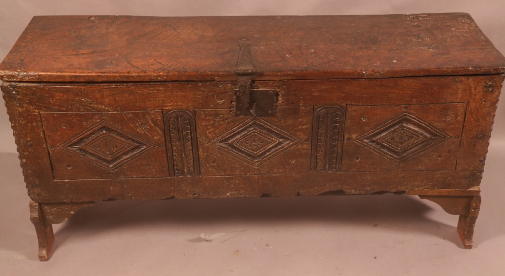 A dark oak early seventeenth-century five-plank coffer featuring carved lozenge panel decoration and hand-forged iron hardware.