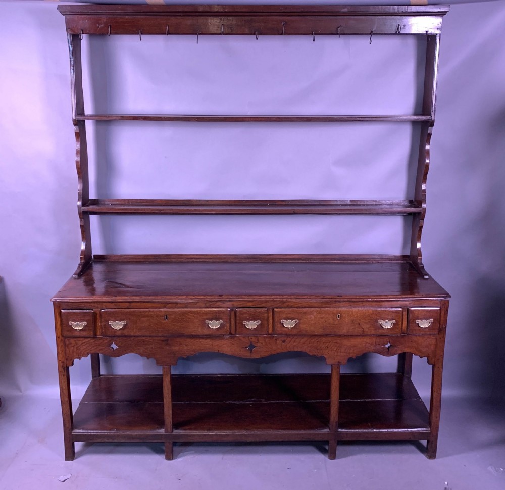 An 18th-century oak Welsh dresser featuring an open rack top with plate hooks, a central base with multiple drawers, and a lower pot board shelf.