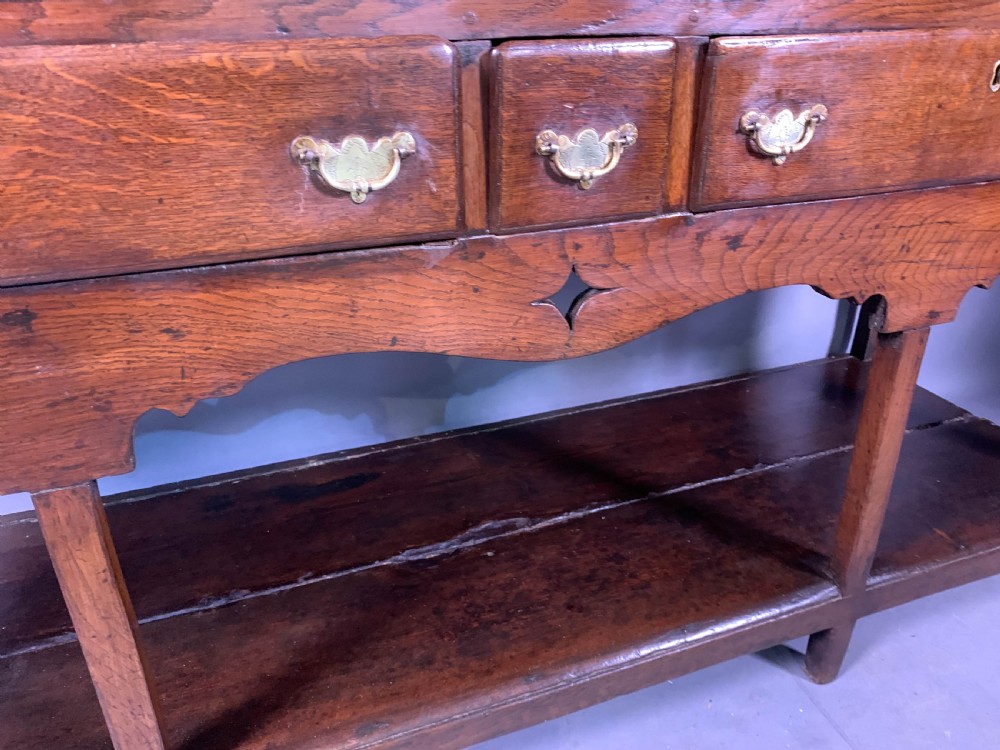 An 18th-century oak Welsh dresser featuring an open rack top with plate hooks, a central base with multiple drawers, and a lower pot board shelf. View III