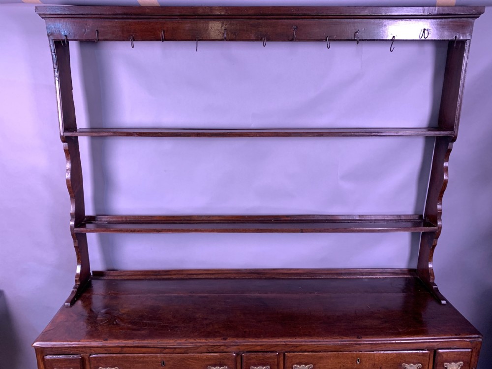An 18th-century oak Welsh dresser featuring an open rack top with plate hooks, a central base with multiple drawers, and a lower pot board shelf. View IV